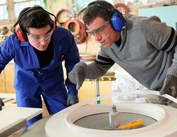 Dos trabajadores en un taller manipulando maquinaria mientras usan protección auditiva.