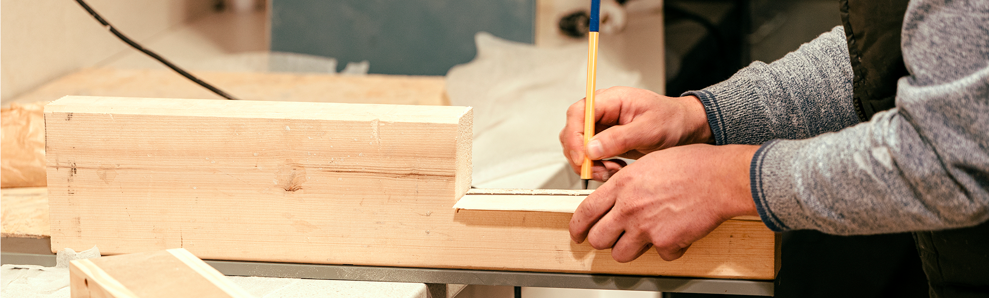Imagen de una persona dibujando sobre una tabla de madera con regla y lápiz, en un entorno de taller