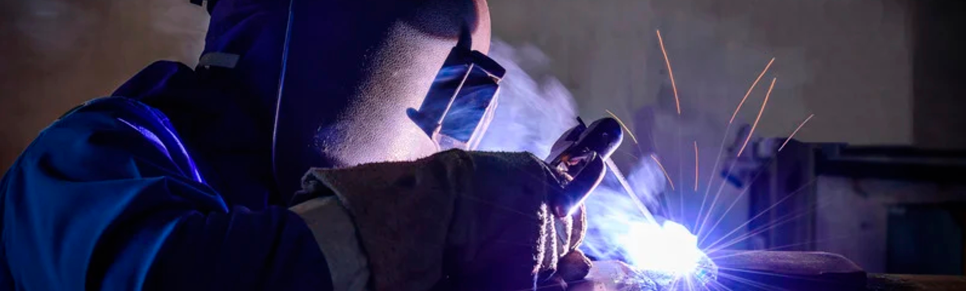 Imagen de una persona soldando una pieza metálica con equipo de protección y generando destellos de luz propios del proceso de soldadura